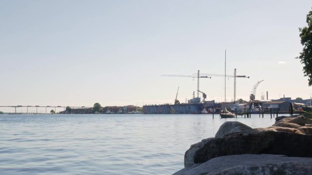A quiet day in Svendborg Sound, a small sailboat moored at a bridge in the foreground of Svendborg Bridge, and a dry dock