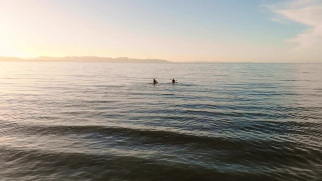 Two women bringing kayaks into the ocean and paddling off into sunset in stunning New Zealand near Abel Tasman National Park.