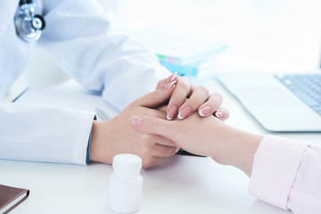Friendly female doctor hands holding patient hand sitting at the desk for encouragement, empathy, cheering and support while medical examination. Just hands over the table.