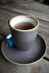 Cup of Black Tea in earthen ware mug with matching saucer on wooden table.  Rustic shabby chic look
