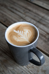 Coffee in cup with leaf design created with milk on the top with rustic blurred wooden background