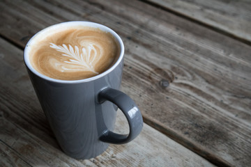 Coffee in cup with leaf design created with milk on the top with rustic blurred wooden background