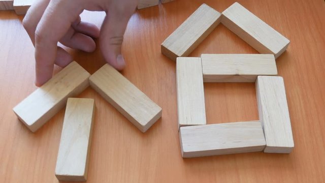 man's hand make house from wooden puzzle over wooden table 