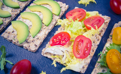 Healthy snack from wholegrain rye crispbread cracker with cherry tomatoes, avocado and salad. Proper nutrition.