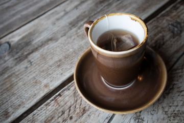 Cup of Black Tea in earthen ware mug with matching saucer on wooden table.  Rustic shabby chic look