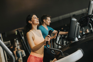 Fototapeta na wymiar Young woman and man on elliptical stepper trainer exercising in gym
