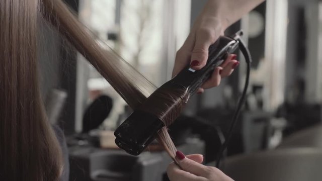 Hairstyling curly hair with iron, close up with smoke, slow motion, second angle