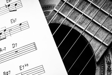 Acoustic guitar and a paper with music score in black and white.