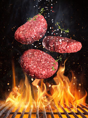 Tasty beef steaks flying above cast iron grate with fire flames.