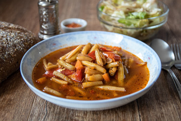 Vegetarian lunch. Green bean soup with tomato sauce and vegetables on wooden table with homemade whole grain bread, iceberg salad and spices