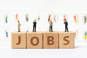 Miniature people, wooden word block "JOBS" with candidates in capsules as backdrop. Human resource concept, recruiting, hiring process.