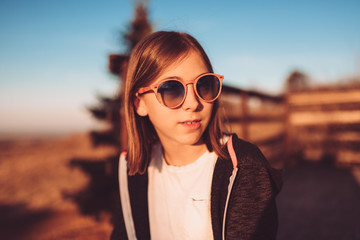 Teenage girl wearing sunglasses sitting outdoor at sunset