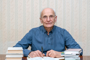 portrait of an elderly professor in glasses sitting at a table with books