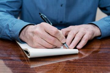 hands of the old man at the table, a man makes a pen writing in a notebook.