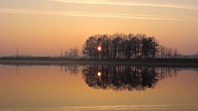 Beautiful timelapse of a sunset reflecting in the lake. The sky is slowly changing its colour from orange to navy blue.