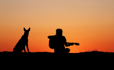 Obraz premium Silhouette girl guitarist on sunset background, silhouette of a dog breed Belgian Shepherd Malinois, happy friends, outdoor