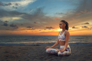 Fototapeta na wymiar Young beautiful woman relaxing in yoga Lotus position on sea sand