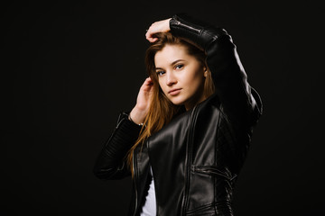 Young caucasian woman wearing a leather jacket and jeans posing on the black background