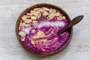 Obraz na płótnie Canvas Red smoothie in coconut bowl with dragon fruit, avocado, almond flakes, coconut chips and chia seeds for breakfast , close up. The concept of healthy eating, superfood