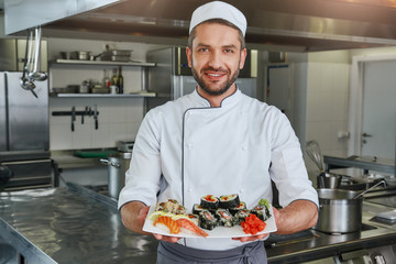 Already ready. Portrait of cheerful chef standing with cooked traditional japanese sushi