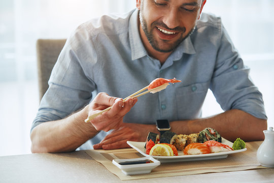 Better food, better mood. Cropped image of smiling handsome businessman eating sushi