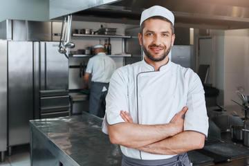 We sell flavors. Smiling attractive chef cook with beard standing with hands folded on the kitchen