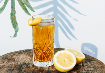 Ice tea in a cocktail glass standing on a wooden table in front of a white wall  outside with...