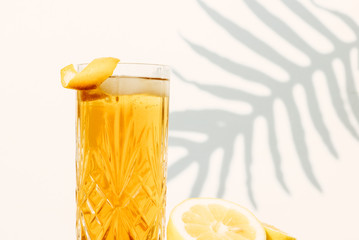 Ice tea in a cocktail glass standing on a wooden table in front of a white wall  outside with shadows of a palm leaf plant in the background