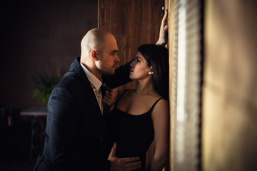 A bald man in a black suit pressed a beautiful dark-haired girl against the wall, the girl holding...