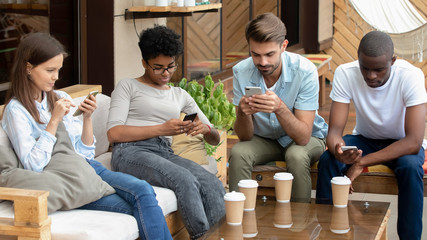 Diverse young friends using social media on phones in cafe