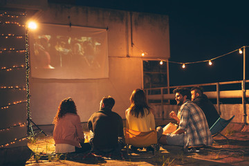 Friends watching a movie on a building rooftop terrace - obrazy, fototapety, plakaty