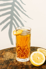 Ice tea in a cocktail glass standing on a wooden table in front of a white wall  outside with shadows of a palm leaf plant in the background