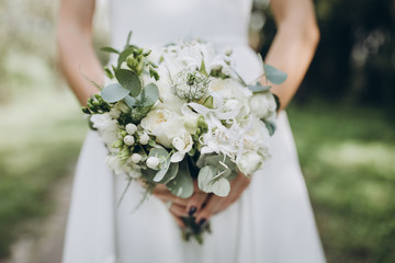 bride in white dress holding a wedding bouquet of flowers and greenery