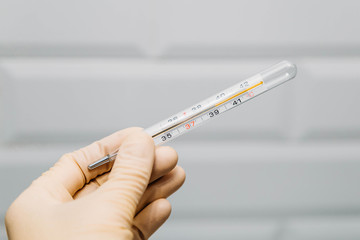 A hand in a medical glove holds a thermometer to measure body temperature. 