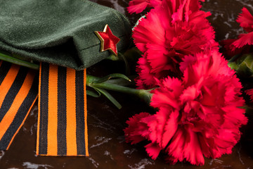 orange ribbon of St. George, two red flowers and a green military uniform close-up