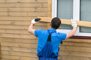 man in coveralls closes windows with boards to protect the house