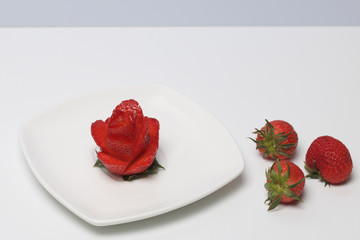 Rose flower made from strawberries. Lies on a saucer. Nearby are other berries.