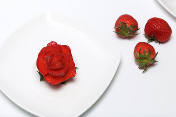 Rose flower made from strawberries. Lies on a saucer.