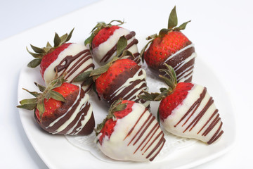 Strawberries glazed in black and white chocolate. Lie on a white plate with a pattern.