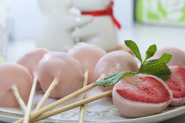 Strawberries in yogurt. Berries are dressed on wooden skewers and dipped in yogurt. Nearby are two halves of dessert. Visible red juicy strawberry flesh. Decorated with mint leaves.