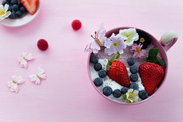 Vegan pink and white Chia pudding in a pink bowl with fresh blueberries, strawberries and flowers
