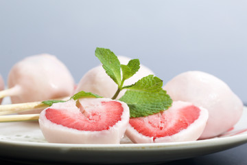 Strawberries in yogurt. Berries are dressed on wooden skewers and dipped in yogurt. Nearby are two halves of dessert. Visible red juicy strawberry flesh. Decorated with mint leaves.