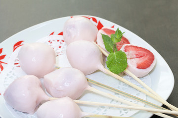 Strawberries in yogurt. Berries are dressed on wooden skewers and dipped in yogurt. Nearby are two halves of dessert. Visible red juicy strawberry flesh. Decorated with mint leaves.