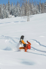 A snowboarder falling into deep snow at the ski resort in a sunny morning