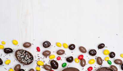 Chocolate Easter eggs and sweets on light wooden background. Top view. Empty space foe text