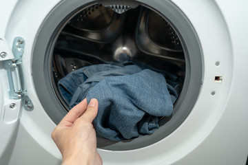 Female hand holding jeans just washed in an automatic washing machine