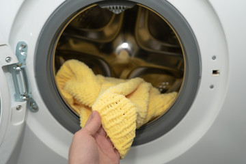 Female hand holding a yellow knitted sweater just washed in an automatic washing machine, hand wash mode for wool
