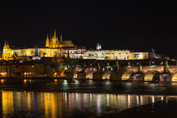 Obraz premium The Prague castle with historic Charles Bridge and Vltava river in the night scene with water reflection. Prague is a popular travel destination. Prague, Czech Republic