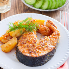 Salmon steak baked with mustard and potatoes on a white plate, square