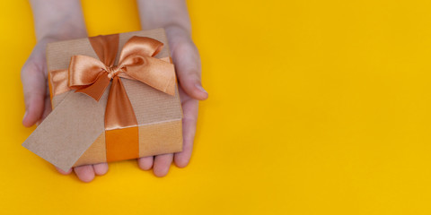 Children hands holding present box on yellow background.